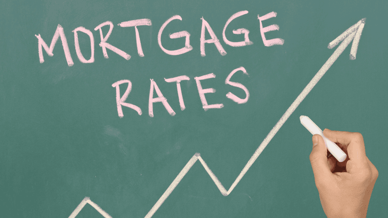 Hand drawing an upward trend beneath the words "Mortgage Rates" on a chalkboard.